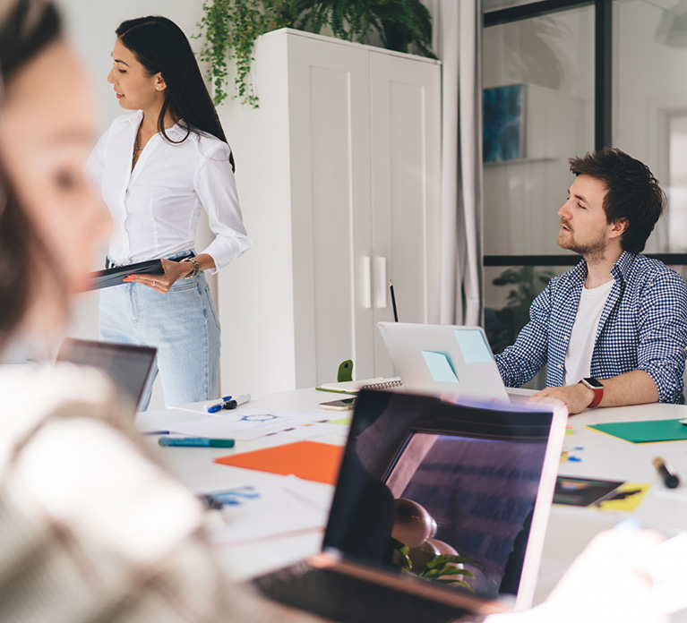 Reunión de equipo con una mujer liderando una discusión mientras sostiene una tableta, con un hombre escuchando atentamente en un entorno de oficina moderno